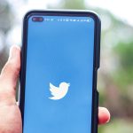 Hand holding smartphone with Twitter app open against blurred natural background.